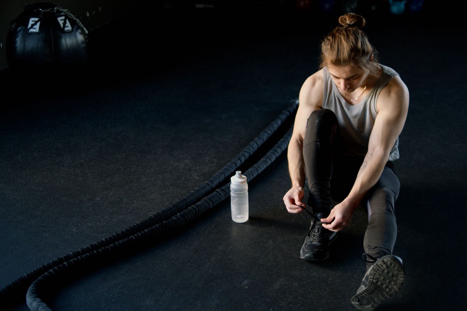 Sportif qui boit à sa gourde en salle de sport entre deux séries