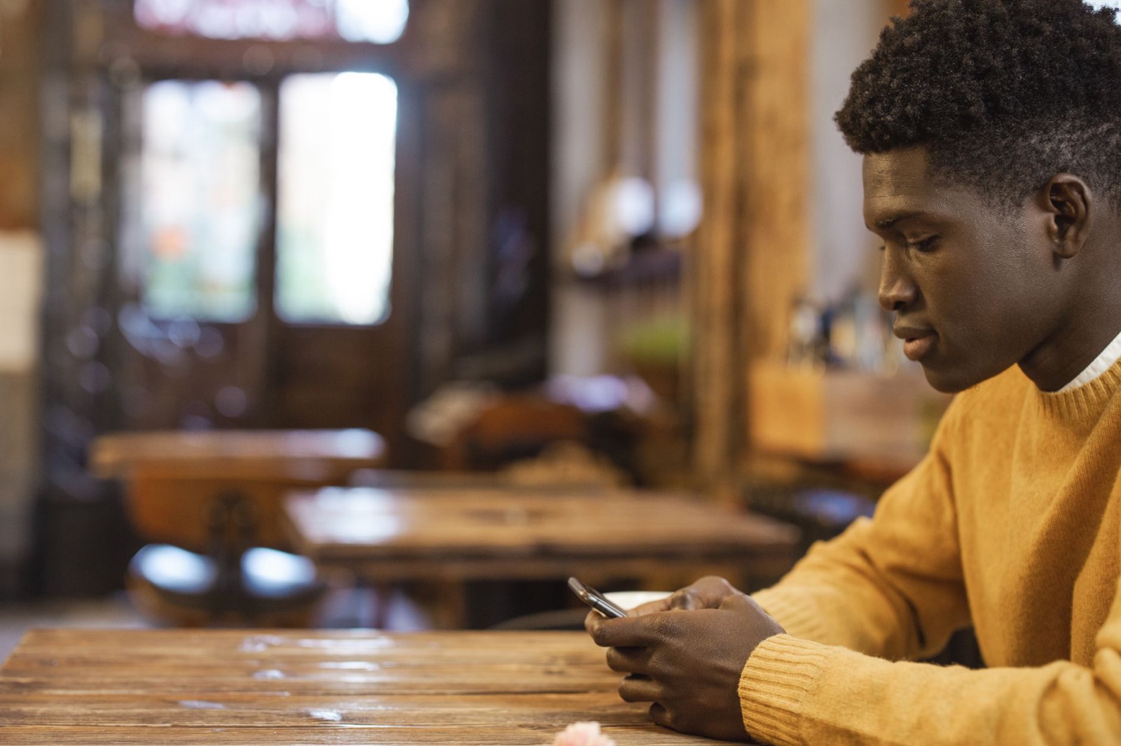 Un jeune homme écrit un message sur son téléphone, assis à la terrasse d'un café